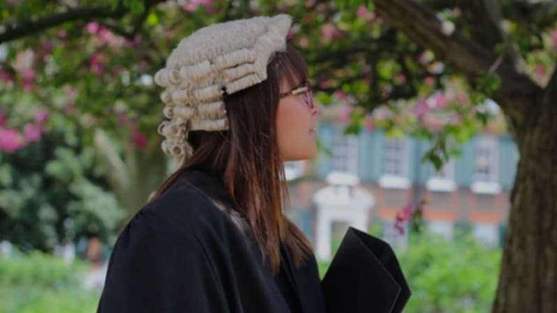 A young woman in a black cloak and barrister's wig stands outside the Inn of Court after admission to the Bar in the UK